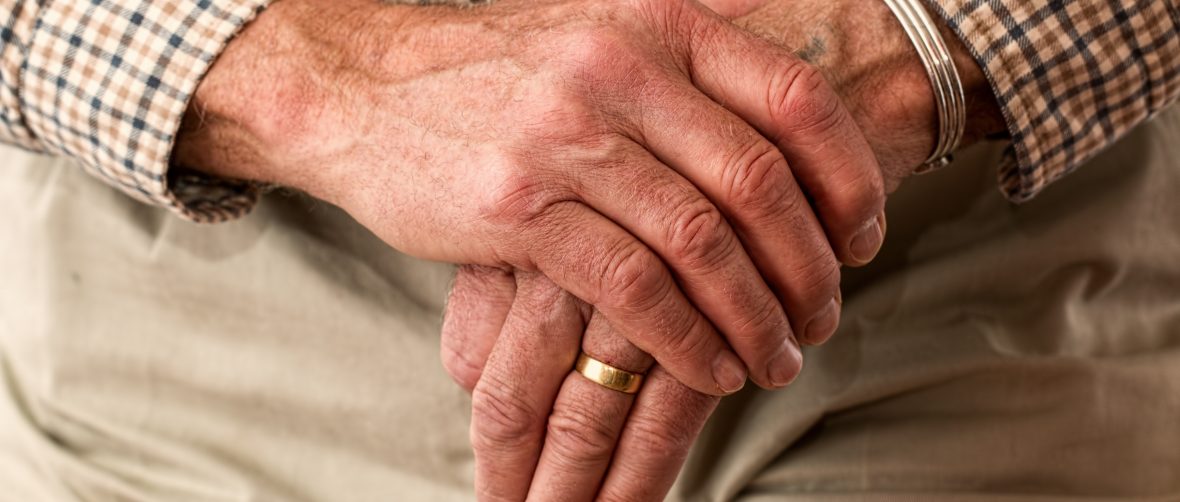 old mans hand holding walking stick with checked shirt